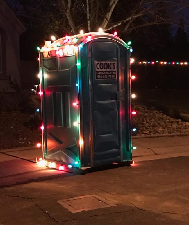 Eine chemische Toilette für Baustellen mit bunten Weihnachtslichtern, es ist Weihnachten für alle
